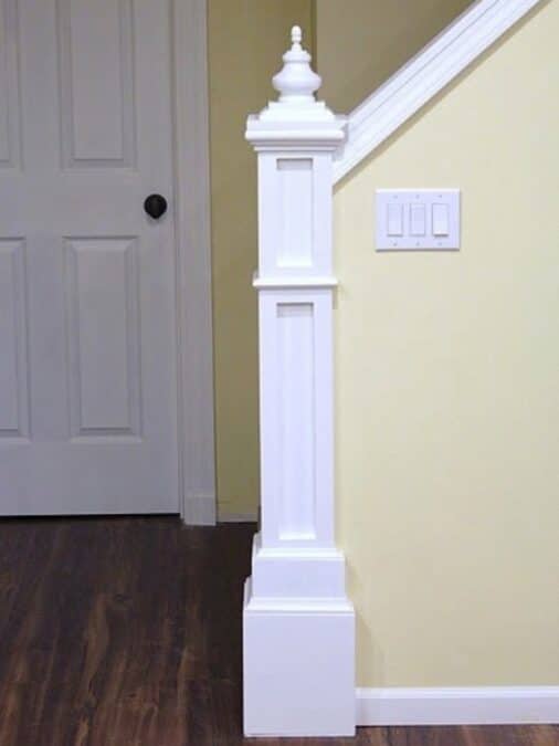 Finished DIY newel post at the end of a stair half wall, painted white with decorative trim and finial