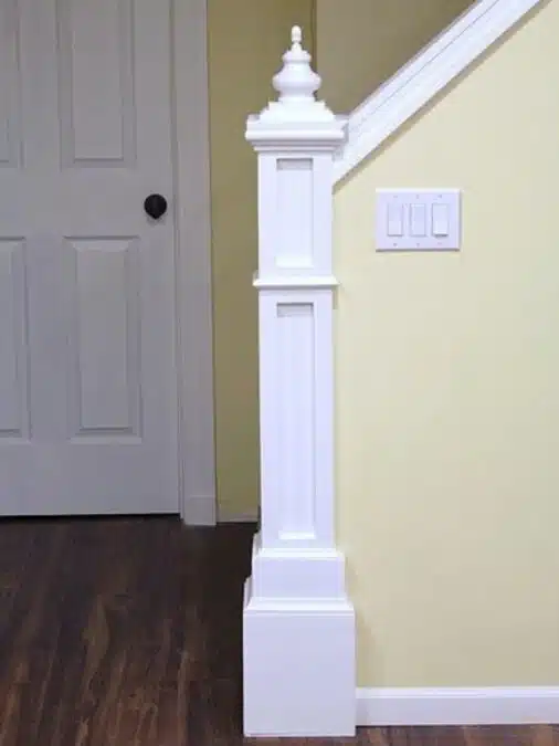 How to Build a Newel Post: DIY Stair Detail 5 Finished DIY newel post at the end of a stair half wall, painted white with decorative trim and finial