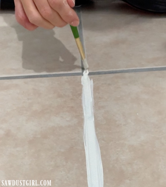 a hand using a paint brush to change grout line color