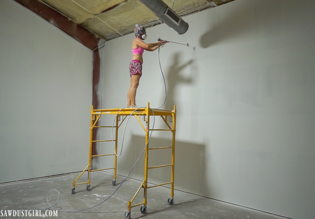 Painting newly installed drywall on scaffolding with an airless sprayer