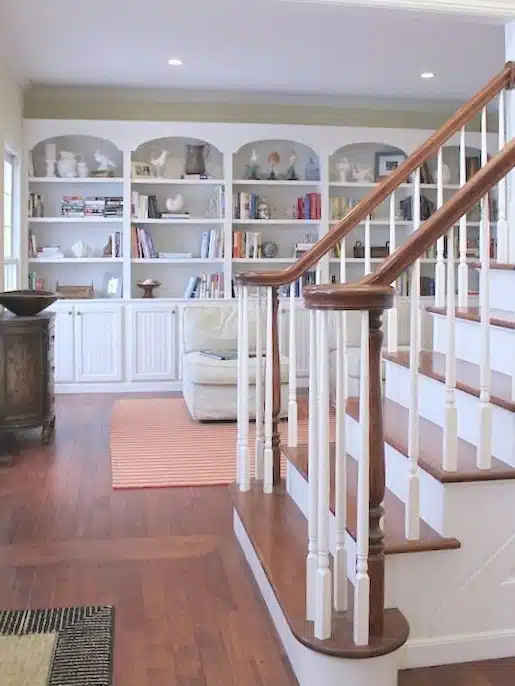 Built-in arched bookcases and reading nook at the base of a staircase in a home library remodel