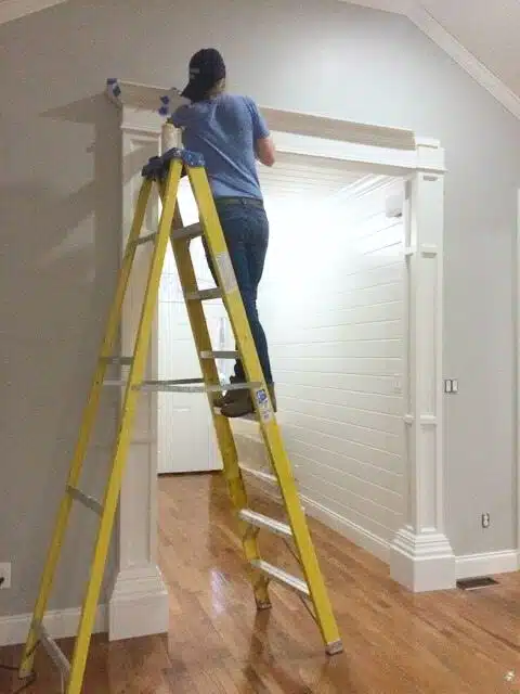 Sandra on ladder adding crown molding to entryway columns